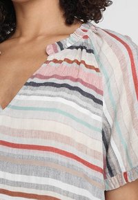 Gestreifte Bluse aus leichtem Stoff mit V-Ausschnitt und gerafften Ärmelabschlüssen. Verfügt über Pastellfarben, darunter pinke, rote, blaue und beige Streifen.