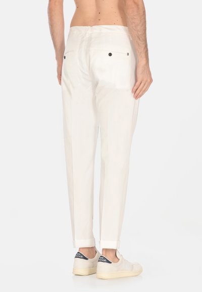 Pantaloni bianchi in cotone con vestibilità rilassata, dotati di orli arrotolati, tasche posteriori e dettagli con bottoni neri. Indossati con sneakers chiare.