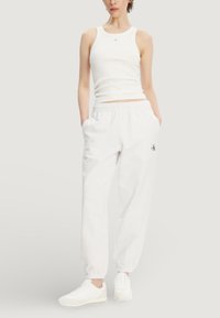 Bílý bavlněný nátělník a odpovídající tepláky s bočními kapsami. Tepláky mají elastické manžety a malou vyšívanou značku na přední straně.