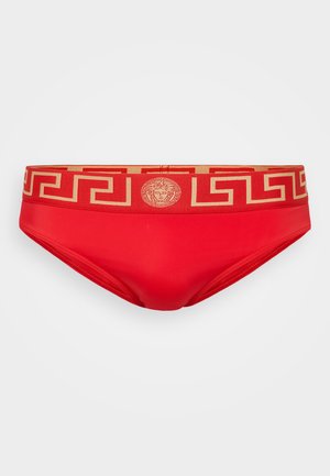 Rote Schwimmslips mit einem goldfarbenen, gemusterten Bund, der ein griechisches Schlüsselmotiv aufweist, und einem zentralen Logo. Glatte Textur und figurnaher Schnitt.