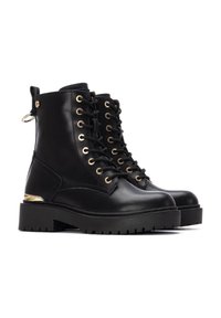 Botas de tobillo de cuero negro con cordones, hardware dorado, suela gruesa y asa en la parte posterior. Cuentan con una textura suave y caña alta.