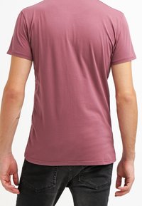 Kurzarm-T-Shirt in staubigem Rosé, leichter Baumwollmischung, taillierte Form, minimale Nahtdetails, glatte Textur, kombiniert mit schwarzen Jeans.