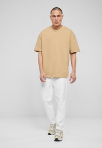Camiseta corta beige de manga corta, de corte holgado y cuello redondo, combinada con pantalones blancos desgastados y zapatillas beige.