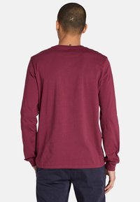 Burgunderfarbendes Langarmshirt mit Rundhalsausschnitt, das eine glatte Textur und ein schlichtes Design aufweist, von hinten gezeigt.
