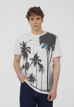T-shirt bianco in cotone con una grafica di una palma nera. Testo "Pacific Dream" stampato in turchese sul lato sinistro superiore. Maniche corte.