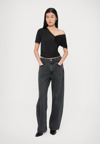 Must off-the-shoulder top kaunistatud roosaga ühel küljel, koos lõdvalt istuvate, kõrge vöökohaga hallide teksapükstega ja teravate mustade kingadega.