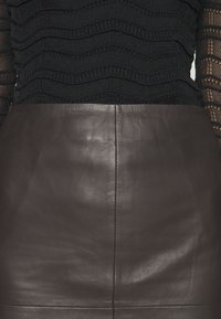 Haut noir texturé à manches longues associé à une jupe en cuir marron foncé taille haute avec des coutures visibles au centre.