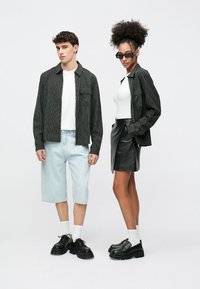 Czarnobiała koszula w paski z kieszenią na piersi, jasnoniebieskie szorty dżinsowe oraz czarna spódnica. Modele noszą czarne buty i okulary przeciwsłoneczne; proste białe bluzki.