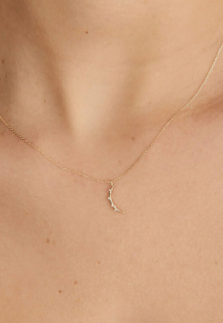 Goldene Halskette mit einem gebogenen Anhänger, der mit kleinen Steinen besetzt ist, zarter Kette und minimalistischen Design. Akzente setzen winzige Kristalle entlang des Anhängers.