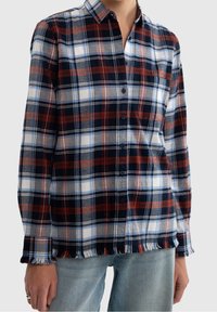 Långärmad rutig skjorta med röd, marinblå och vit rutmönster. Detaljer inkluderar knappstängning och fransad fåll. Tillverkad av mjukt tyg.