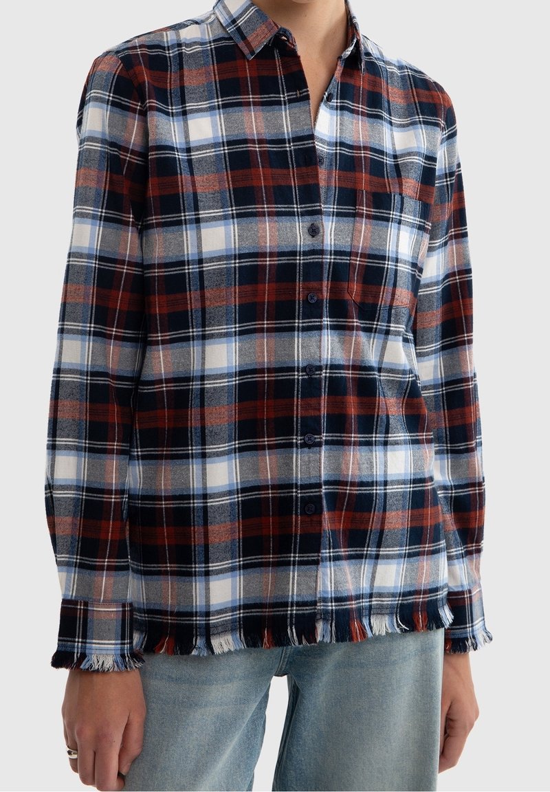 Långärmad rutig skjorta med röd, marinblå och vit rutmönster. Detaljer inkluderar knappstängning och fransad fåll. Tillverkad av mjukt tyg.