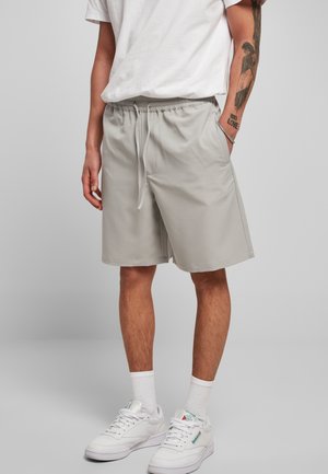 Pantalones cortos deportivos gris claro con cintura elástica, cordón ajustable, bolsillos laterales y tela suave. Combinados con zapatillas blancas y calcetines hasta la mitad de la pierna.