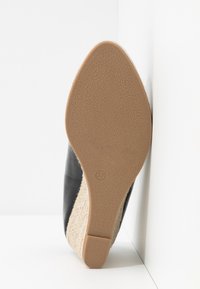 Zapato de cuña de cuero negro con suela de goma texturizada y un acento natural de yute tejido; tamaño marcado como 37 en la parte inferior.
