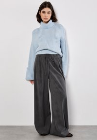 Maglione collo alto lavorato a maglia blu chiaro con maniche ampie, abbinato a pantaloni larghi grigio antracite a righe e scarpe nere.