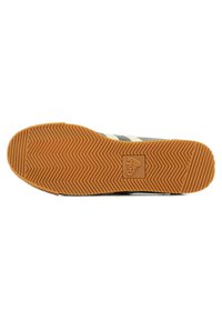 Suola di sneaker con un motivo a zigzag, realizzata in gomma naturale, parte superiore scura con tre strisce bianche e stampa del logo.