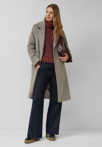 Szary wełniany płaszcz z klapami, zestawiony z bordowym golfem i ciemnymi, szerokimi spodniami dżinsowymi. Całość dopełniają czarne botki na platformie.