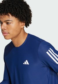 Navy sininen urheilupaita, joka on valmistettu teksturoidusta kankaasta. Paidassa on valkoinen Adidas-logo rinnassa ja kolme valkoista raitaa olkapäällä.