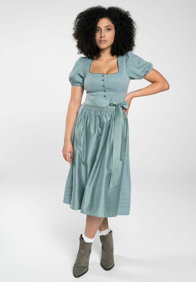 Een teal jurk met puffed sleeves, vierkante halslijn en knoopdetails; heeft een gestrikte taille en een vloeiende rok. Gecombineerd met grijze enkelboots.