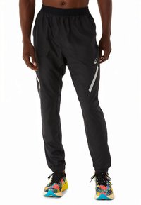 Pantalon de sport noir à coupe décontractée, taille élastique et accents réfléchissants sur les côtés, associé à des baskets colorées à motifs.