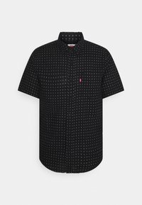 Chemise noire à manches courtes avec boutons, petits motifs circulaires blancs et une étiquette rouge avec le logo Levi's sur la poche poitrine gauche.