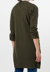 Olivově zelený kardigan z texturované pleteniny, s vyhrnutými rukávy a dlouhým, volným střihem. Jednoduchý design bez viditelných vzorů.
