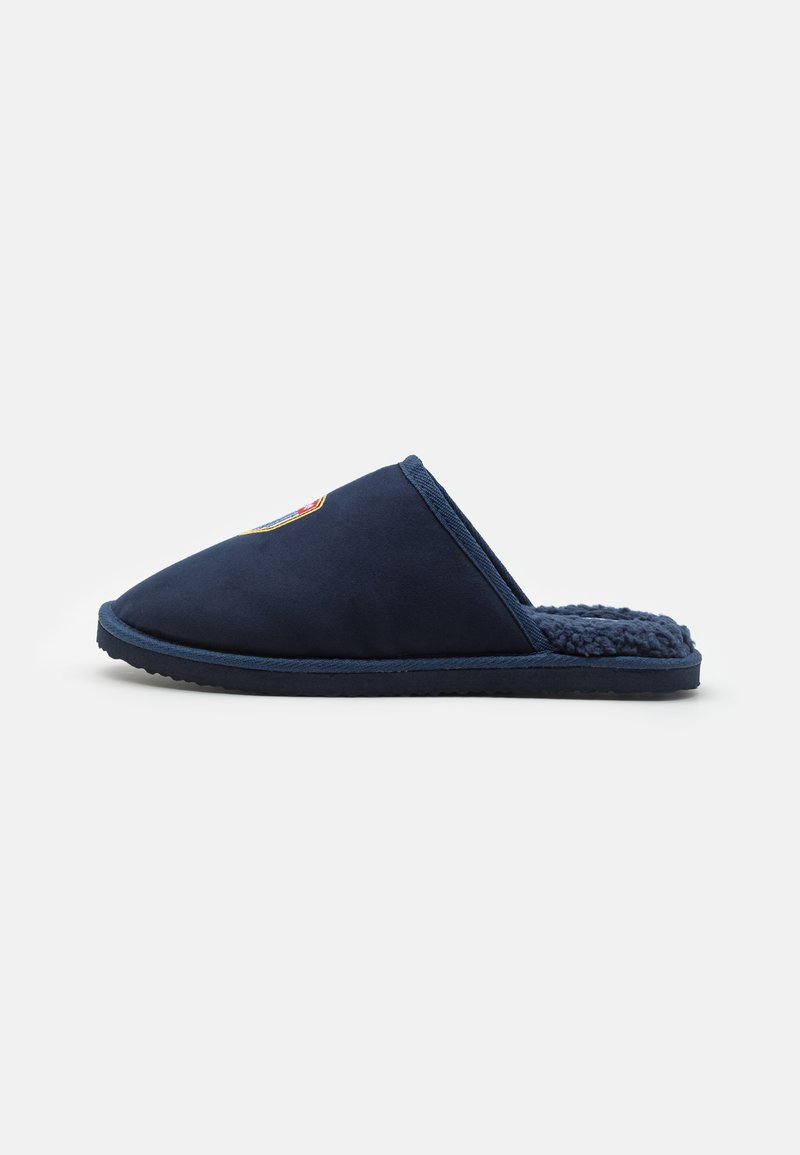 Marineblå slip-on tøfler med en myk, teksturert innvendig og en spiss tådesign. Har detaljert logo sydd på oversiden.