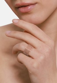 Roze gouden ring met een gestructureerd oppervlak dat gelaagde, gedraaide patronen vertoont. Draagt op een hand met naturel nagels, en toont een elegant ontwerp.