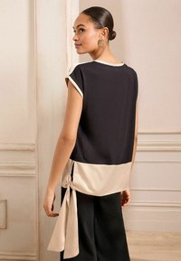 Top senza maniche in nero e crema con una vestibilità ampia, caratterizzato da un dettaglio annodato all'orlo e da una texture liscia.