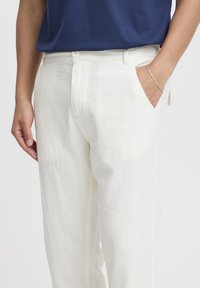 Witte linnen broek met een rechte snit, voorzien van zijzakken en een subtiele textuur. Gepaard met een marineblauwe shirt.