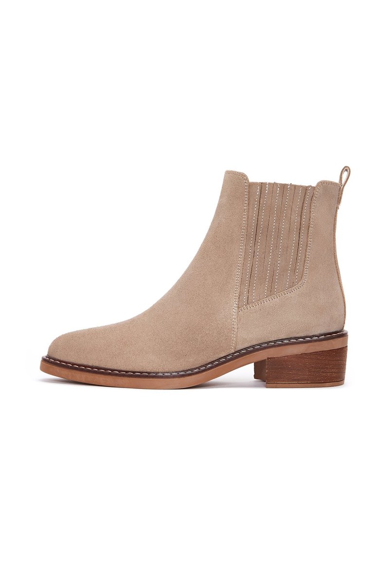 Stivale alla caviglia in suede beige con punta rotonda, pannelli laterali elasticizzati e tacco basso impilato. Presenta cuciture decorative e un tassello per il sollevamento.