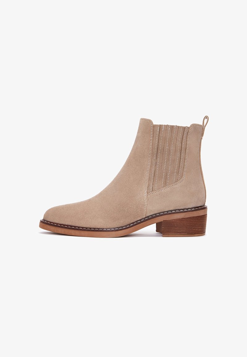 Stivale alla caviglia in suede beige con punta rotonda, pannelli laterali elasticizzati e tacco basso impilato. Presenta cuciture decorative e un tassello per il sollevamento.