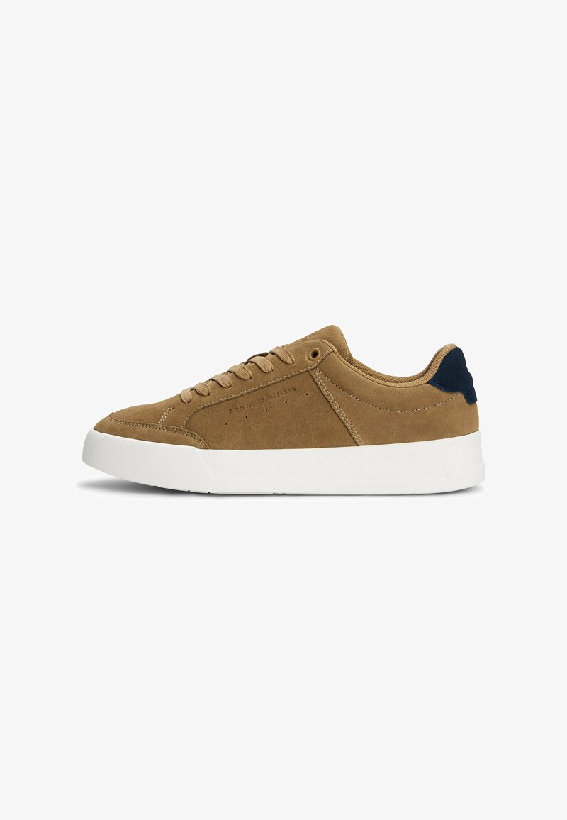 Sneaker in suede marrone con suola in gomma bianca, punta tonda, design perforato e accentuazione sul tallone di colore blu scuro. Presenta lacci piatti e branding.