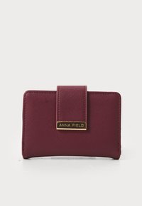 Portofel burgundy cu o suprafață texturată, având o plăcuță logo rectangulară aurie și închidere magnetică. Formă compactă rectangulară.