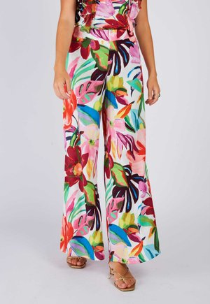 Szerokie spodnie z żywym, wielokolorowym tropikalnym kwiatowym nadrukiem, noszone z otwartymi sandałami na paski.