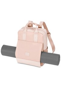 Zaino rosa pallido con doppie maniglie e cintura regolabile, presenta una tasca frontale e tiene un tappetino da yoga grigio sul lato.