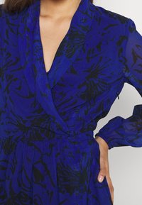 Blå klänning med svart blommönster, med V-ringning, insvängd midja och långa genomskinliga ärmar med elastiska manschetter.