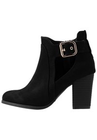 Zwarte suède enkellaars met een ronde neus, zijsnedes en een gouden gespdetail bij de enkel. Voorzien van een geprofileerde blokhak.