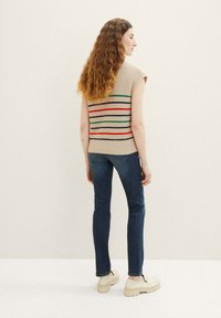 Haut sans manches beige tricoté avec des rayures horizontales multicolores, associé à un jean bleu foncé et des chaussures à plateforme crème.