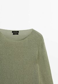 Pull en maille vert olive clair avec un col rond. Il présente une texture douce et des détails de couture subtils le long des épaules.