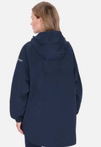 Sötétkék vízálló dzseki kapucnival, rugalmas mandzsettákkal és laza szabással. Hátul yoke rész, sima, texturált anyagból készült.