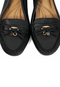 Zwarte leren loafers hebben een ronde neus, een decoratieve strik met goudkleurige hardware en een gestructureerd oppervlak op het bovenwerk en gestikte randen.