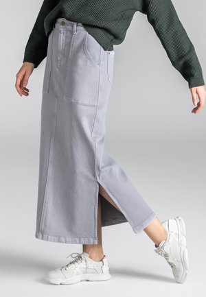 Hellgrauer Denimrock mit zwei vorderen Taschen, geradem Schnitt und seitlichen Schlitzen für Bewegungsfreiheit, kombiniert mit weißen Sportschuhen.