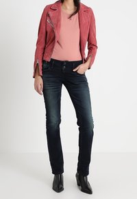 Röd mockajacka för motorcykel med dragkedjedetaljer, i kombination med mörka jeans och svarta klackstövlar. Enkel rosa topp under.