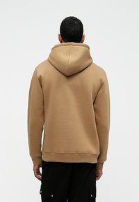 Φόρμα με κουκούλα σε ανοιχτό καφέ χρώμα, κατασκευασμένη από μαλακό ύφασμα, με χαλαρή εφαρμογή, ριμπ μανσέτες και καγκουρό τσέπη.