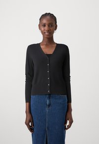 Svart cardigan med V-hals, lange ermer, knappelukking foran og myk tekstur, kombinert med et denimskjørt som har splitt foran.