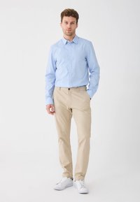 Šviesiai mėlyna marškiniai su sagomis, smėlio spalvos kelnės ir balti sportbačiai. Apranga pasižymi klasikiniu kirpimu, lygiu audiniu ir paprastu dizainu.