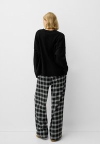 Fekete kötött pulóver kerek nyakkivágással. Laid-back stílus, széles lábú fekete-fehér kockás nadrággal párosítva. Egyszerű design, bordázott mandzsettákkal.