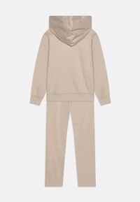 Béžový bavlnený teplákový komplet s kapucňou a slim-fit nohavicami. Hladká textúra s rebrovanými manžetami a pásom. Jednoduchý dizajn.