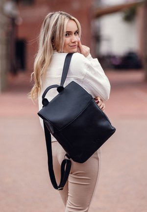 Schwarzer Leder-Rucksack mit einem strukturierten Design, flachem Deckel und zwei oberen Griffen. Verstellbarer Schultergurt. Glatte Textur mit minimalen Akzenten.