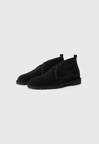 Stivaletti neri in suede con una superficie liscia, punta arrotondata e suola in gomma. Presentano una lacing minima e un passante sul tallone.